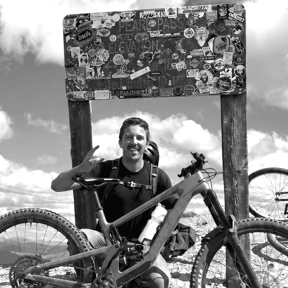 Daniel smiling with a mountain bike beneath the Pearl Pass sign