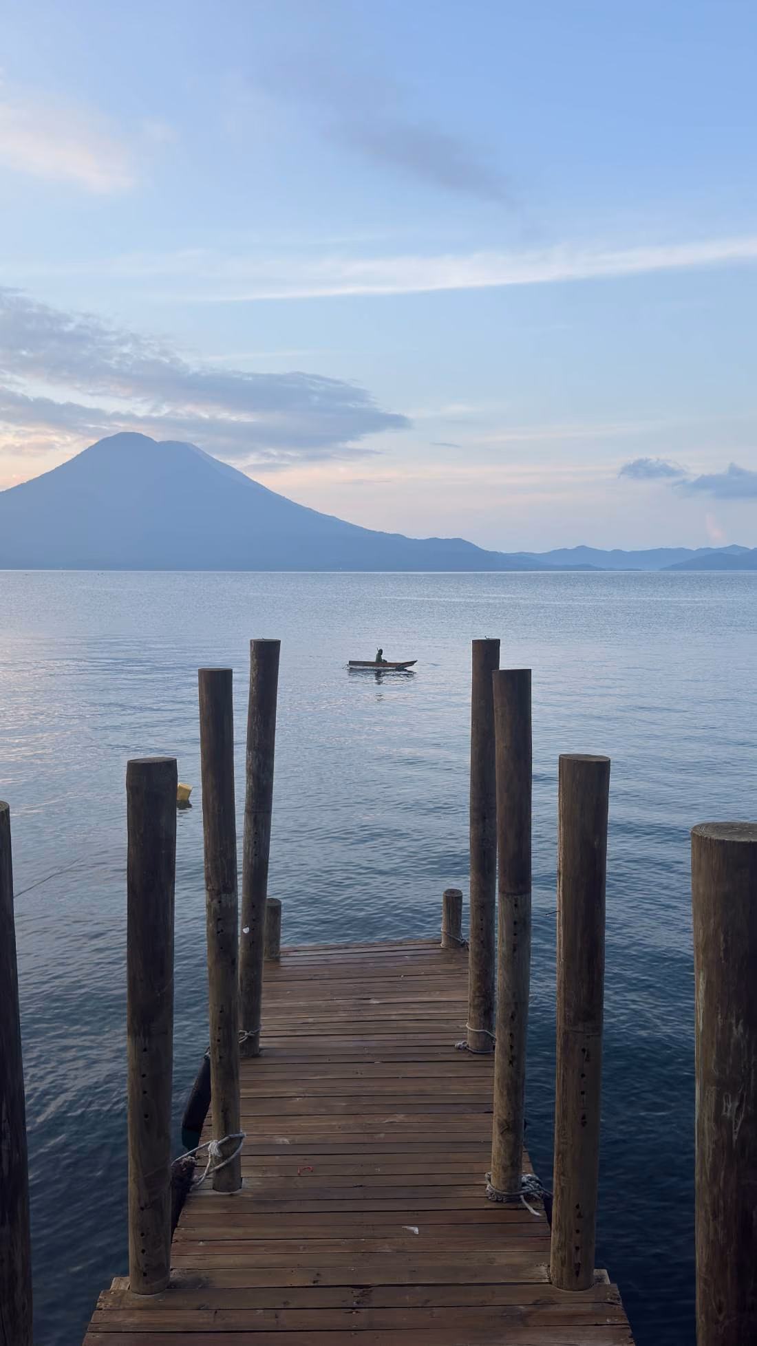 A wooden dock leading into a calm lake with mountains in the distance