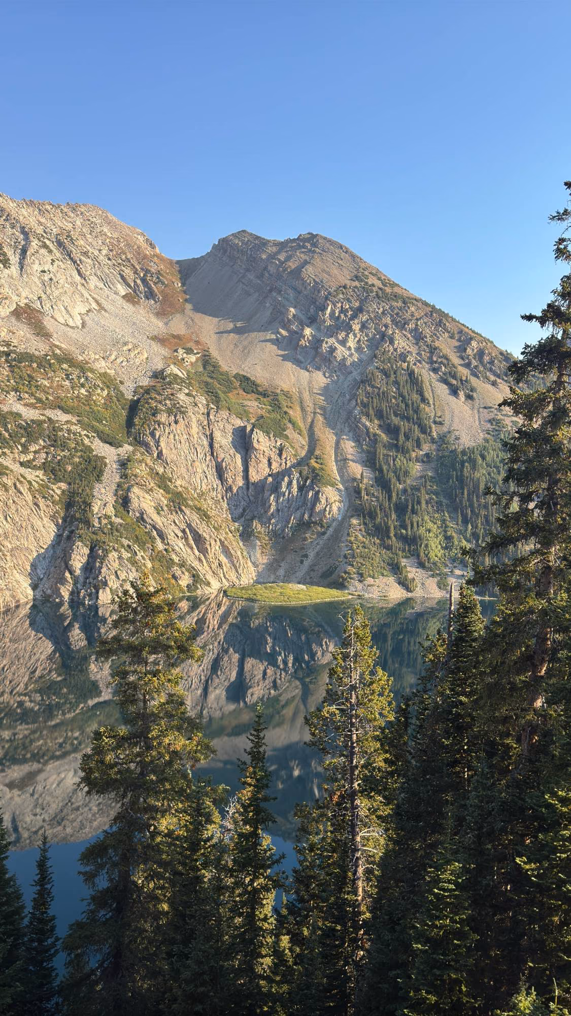 An alpine lake reflecting a rocky mountain peak, framed by evergreens.